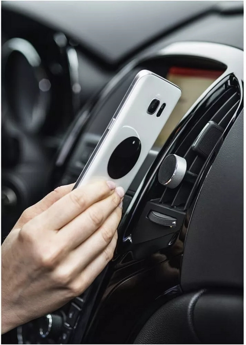 Eine Hand befestigt ein Smartphone mit einem kreisförmigen Magneten an der HandyOase Hama Universal Kfz-Halterung (Schwarz) für Lüftungsgitter im Auto.